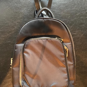 May include: A black backpack with gold zips and a small front pocket. The backpack has a top handle and adjustable shoulder straps.