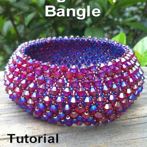 May include: A close-up of a red and blue beaded bangle bracelet. The bracelet is made with small, faceted beads that create a shimmering effect. The text "Bling Me Up Bangle" and "Tutorial by Juelle's Designs" is visible in the image.