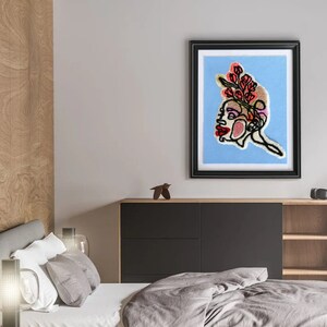 May include: A framed embroidery artwork depicting a profile of a person with a floral crown. The embroidery is done in shades of pink, red, and brown on a light blue background.