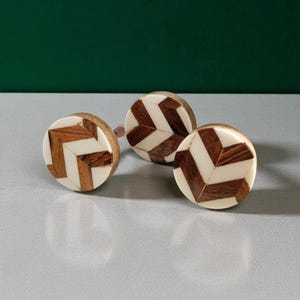 Peut inclure: Trois boutons de meuble décoratifs en bois avec un motif en chevrons. Les boutons combinent du bois clair, du bois foncé et des accents blancs. Les boutons ronds ont un design simple et élégant, adapté à divers styles de meubles.