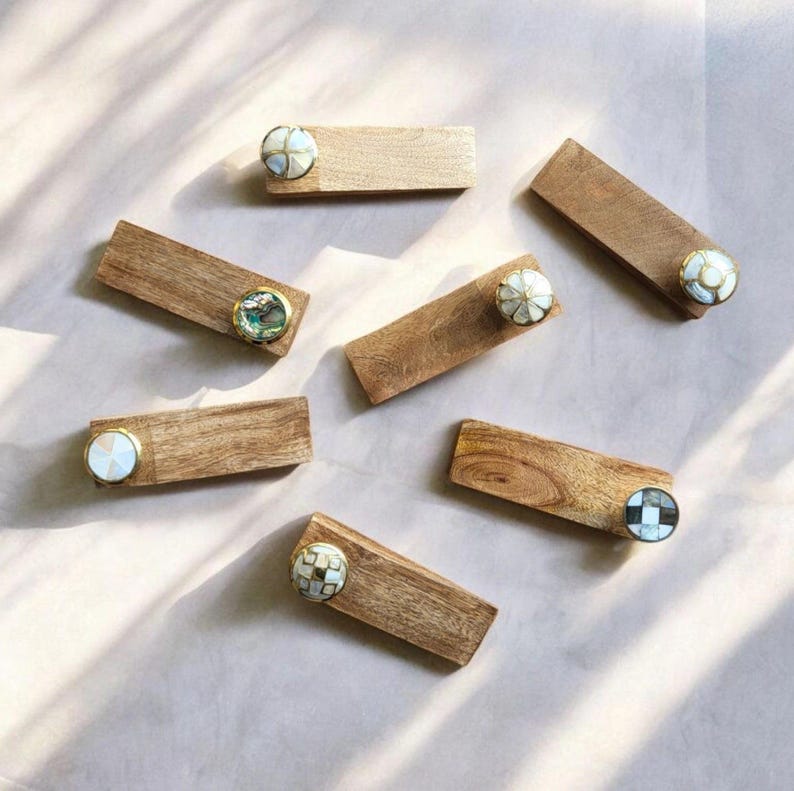 Pu&ograve; includere: Set di sei fermaporta in legno con pomelli decorativi. Ogni pomo &egrave; realizzato con materiali diversi, tra cui conchiglia e mosaico. I fermaporta sono di colore marrone chiaro.