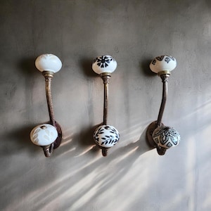 Puede incluir: Tres ganchos de pared decorativos con pomos de cerámica. Cada pomo presenta un diseño floral diferente en blanco y negro.