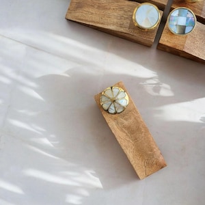 Pu&ograve; includere: Un set di quattro fermaporte in legno con pomelli decorativi in madreperla e ottone. I fermaporte sono rettangolari e hanno una finitura in legno naturale.