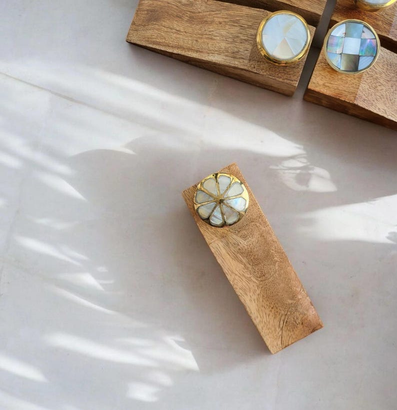 Pu&ograve; includere: Un set di quattro fermaporte in legno con pomelli decorativi in madreperla e ottone. I fermaporte sono rettangolari e hanno una finitura in legno naturale.