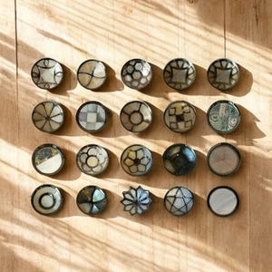 Könnte beinhalten: Zwanzig dekorative runde Schalen mit verschiedenen geometrischen und floralen Mustern in Schwarz-, Weiß- und Grautönen. Die Schalen sind aus Perlmutt gefertigt und haben eine glänzende Oberfläche.