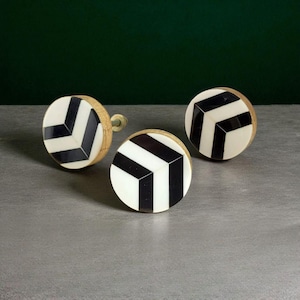 Puede incluir: Tres tiradores decorativos para armarios con un patrón geométrico de chevrón en blanco y negro. Los tiradores tienen una base redonda de madera y un tornillo de latón. El diseño es moderno y complementaría varios estilos de muebles.