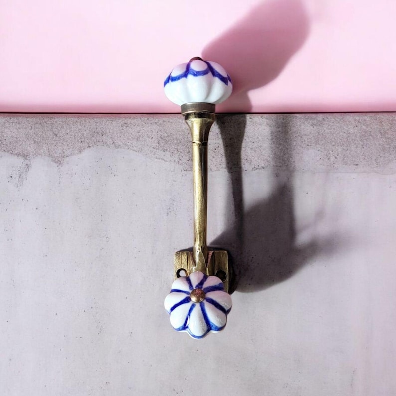 May include: A brass hook with a white ceramic knob with blue trim. The knob is shaped like a flower.