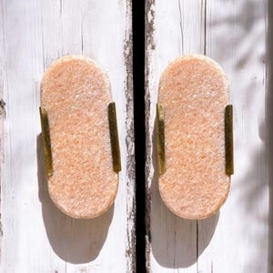 Könnte beinhalten: Zwei hellrosa, ovale Türklinken mit goldenen Metallakzenten an einer weißen Holztür.