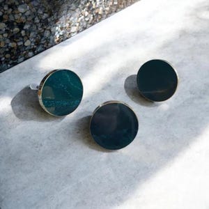 Può includere: Tre pomelli rotondi per armadi, di colore verde scuro, con effetto marmo e bordo dorato.