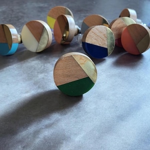 Könnte beinhalten: Sortiment an bunten runden Holzknöpfen mit geometrischen Mustern und goldenen Akzenten. Die Knöpfe sind aus Holz und haben eine Vielzahl von Farben, darunter Blau, Grün, Gelb, Rot und Weiß.