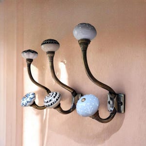May include: Five decorative hooks with ceramic knobs in various patterns. The hooks are made of metal and have a brass finish. The knobs are white with blue and black accents.