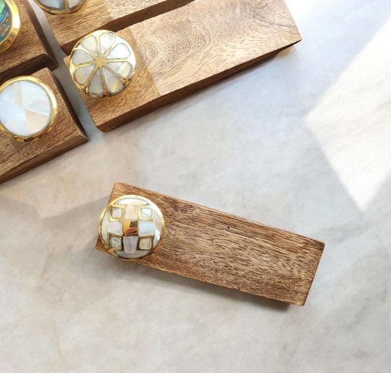 Pu&ograve; includere: Set di quattro fermaporte in legno con pomelli rotondi decorativi con intarsi in conchiglia bianca e dorata. I pomelli hanno motivi diversi.