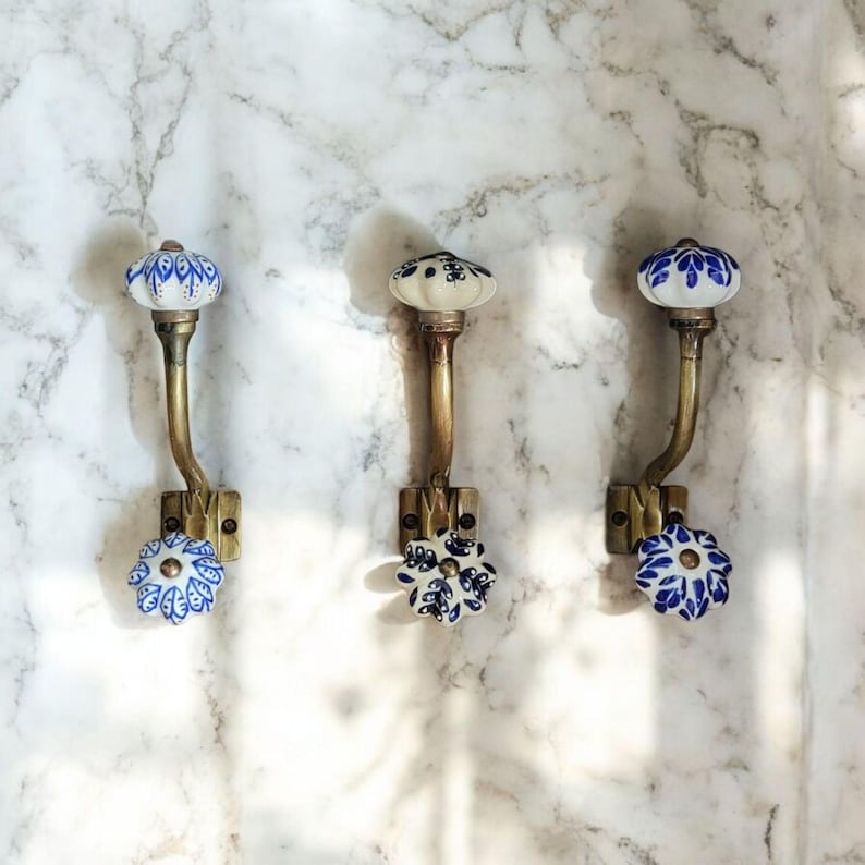 May include: Three decorative wall hooks with blue and white ceramic knobs. The hooks are made of brass and have a simple, elegant design.