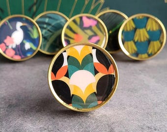 May include: Set of six round gold cabinet knobs with colorful geometric patterns. The patterns include a white bird on a blue background, green and yellow leaves, pink and yellow flowers, green and yellow stripes, and a black and white geometric pattern.