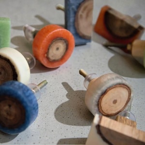 May include: A collection of colorful cabinet knobs with a wood grain design. The knobs are in various colors, including orange, blue, green, and white. Each knob has a clear, cylindrical stem for mounting. The knobs are made of resin and wood.