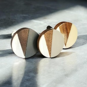 Op de afbeelding: Drie ronde houten knoppen met een geometrisch ontwerp. Elke knop is gemaakt van twee verschillende tinten hout, waardoor een uniek patroon ontstaat. De knoppen zijn perfect om elke kamer een vleugje moderne stijl te geven.