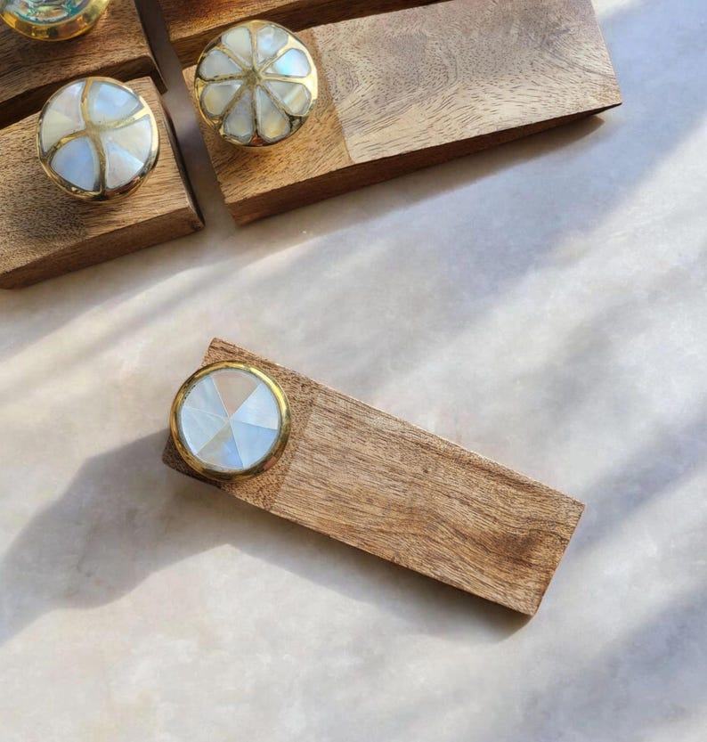 Pu&ograve; includere: Un set di quattro tiretti per cassetti in legno con intarsi in madreperla bianca e dorata. I tiretti sono disposti su una superficie in legno.
