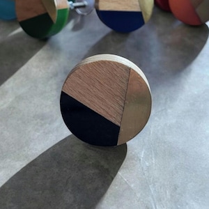 Puede incluir: Un pomo redondo de madera con un diseño geométrico. El pomo está hecho de madera con detalles en negro, dorado y marrón.