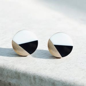 May include: A pair of gold-toned earrings with black and white geometric designs. The earrings are round and have a modern, minimalist style.
