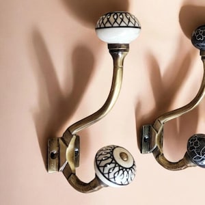 Peut inclure: Deux crochets en métal doré avec des boutons en céramique. Un bouton est blanc avec des motifs géométriques noirs, l'autre est noir avec des motifs floraux blancs.