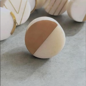 May include: A collection of decorative cabinet knobs. The knobs are white with gold accents and a two-tone design of brown and white. Some knobs have gold stripes or chevron patterns.