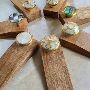 Pu&ograve; includere: Set di otto fermaporta in legno con intarsi rotondi decorativi di vari colori e motivi. Gli intarsi sono in madreperla e sono incastonati in ottone.