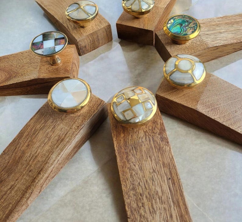 Pu&ograve; includere: Set di otto fermaporta in legno con intarsi rotondi decorativi di vari colori e motivi. Gli intarsi sono in madreperla e sono incastonati in ottone.