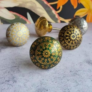 Könnte beinhalten: Sortiment an dekorativen Schrankknöpfen mit komplizierten Mandala-Designs. Die Knöpfe sind in Gold, Schwarz, Weiß und Grün lackiert.