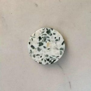 May include: A round, white coaster with a black and green terrazzo pattern.