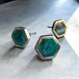 May include: Three hexagonal cabinet knobs with a silver and gold finish. The center of each knob features a vibrant green stone with a unique pattern. The knobs are designed for easy installation and add a touch of elegance to any furniture piece.