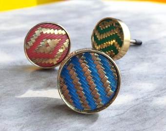 May include: Three decorative cabinet knobs with woven patterns. One knob is red with gold accents, another is green with gold, and the third is blue with gold. The knobs have a circular design and a gold-colored base.