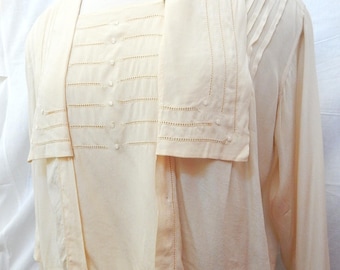 May include: A cream-colored blouse with a decorative collar and button-up front. The blouse has a delicate embroidered design and a slightly cropped length.