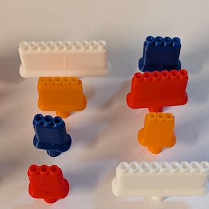 May include: An assortment of colorful plastic toy blocks in various shapes and sizes. The blocks are in shades of white, orange, red, and blue. The image is taken on a white background.