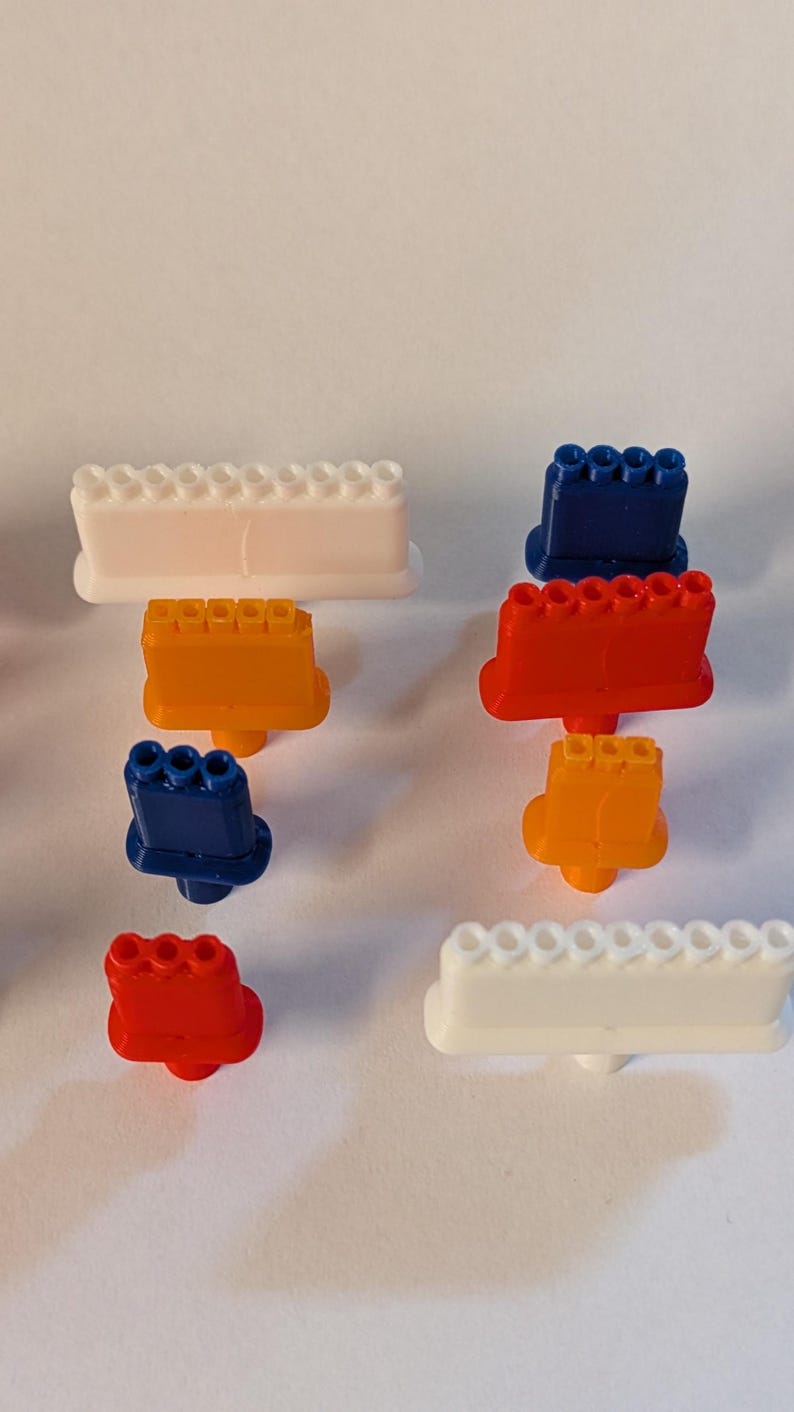 May include: An assortment of colorful plastic toy blocks in various shapes and sizes. The blocks are in shades of white, orange, red, and blue. The image is taken on a white background.