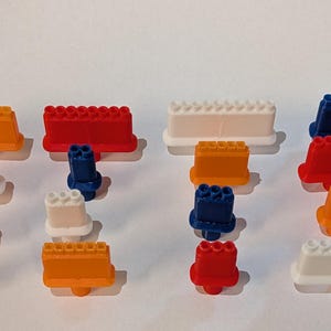 May include: A collection of colorful plastic toy building blocks in various shapes and sizes. The blocks are in shades of orange, red, white, and blue. The image is taken from a top-down perspective.
