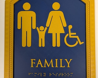 May include: A rectangular sign with a gold frame and a blue background. The sign features yellow silhouettes of a family, including a person in a wheelchair. The word "FAMILY" is printed in yellow, along with Braille text.