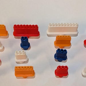 May include: An assortment of colorful plastic toy building blocks in various shapes and sizes. The blocks are in shades of orange, red, white, and blue. Some blocks have a row of circular studs, while others have multiple connector holes.