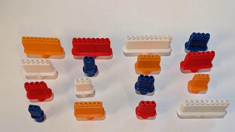 May include: An assortment of colorful plastic toy building blocks in various shapes and sizes. The blocks are in shades of orange, red, white, and blue. Some blocks have a row of circular studs, while others have multiple connector holes.