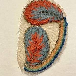 May include: Embroidered patch with a feather design. The patch features orange and blue threadwork, outlined with gold metallic thread. A rainbow-coloured border adds a decorative touch. The patch is on a beige fabric.