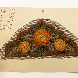 May include: Embroidered design on aged paper. The design features three orange rosettes with gold bead centers, surrounded by green and brown stitching. The design is outlined with black lace. Handwritten text and the number 3 are visible.