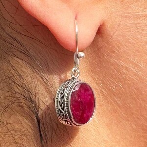 Op de afbeelding: Zilveren oorhangers met een ronde, rode edelsteen in een zilveren zetting. De oorbellen hebben een delicaat, versierd ontwerp.