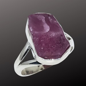 K&ouml;nnte beinhalten: Ein Silberring mit einem gro&szlig;en, roh geschnittenen, purpurrosa Edelstein. Der Stein ist in einem polierten Silberband mit geteiltem Schaftdesign gefasst. Der Ring zeigt eine nat&uuml;rliche, organische &Auml;sthetik.