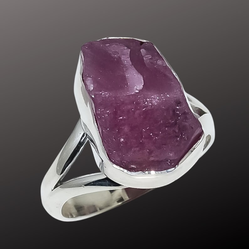 K&ouml;nnte beinhalten: Ein Silberring mit einem gro&szlig;en, roh geschnittenen, purpurrosa Edelstein. Der Stein ist in einem polierten Silberband mit geteiltem Schaftdesign gefasst. Der Ring zeigt eine nat&uuml;rliche, organische &Auml;sthetik.