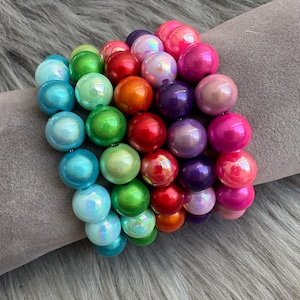 Könnte beinhalten: Ein Stapel bunter Armbänder aus irisierenden runden Perlen. Die Armbänder sind in Blautönen, Grün, Rot, Orange, Lila und Pink.