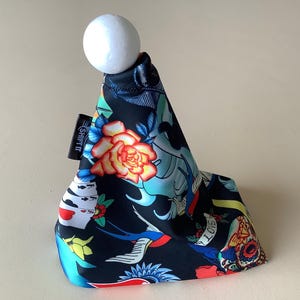 Puede incluir: Una funda de palanca de cambios negra con un diseño colorido de estilo tatuaje que presenta una rosa, un pájaro, una calavera y cartas de juego. La funda tiene una bola blanca en la parte superior y el texto "SHIFT" en el lateral.