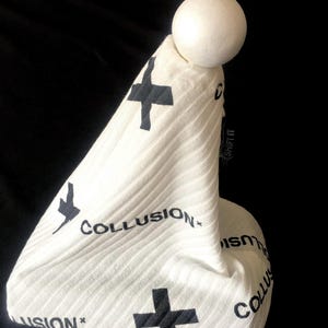 May include: White fabric cone with black crosses and the text "COLLUSION*" printed on it. A white sphere sits on top of the cone.