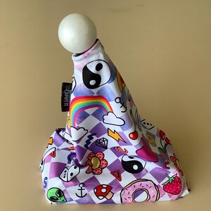 Peut inclure: Un couvre-pommeau de levier de vitesse à carreaux blancs et violets avec un arc-en-ciel, des nuages, un beignet, une fleur, un symbole yin yang, un dé, une ancre, un champignon, un extraterrestre et une fraise. Le texte "Shift It" est imprimé sur le côté du couvre-pommeau.