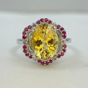 May include: A silver ring with a large oval yellow gemstone surrounded by a halo of small red gemstones.