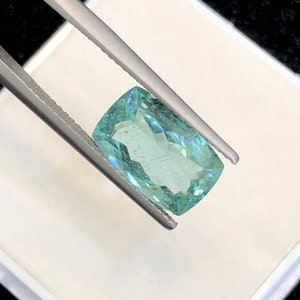 May include: A light green gemstone with a rectangular shape, held by tweezers against a white background.