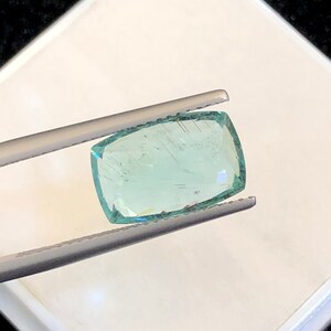 May include: A light green gemstone with a rectangular shape, held in tweezers.